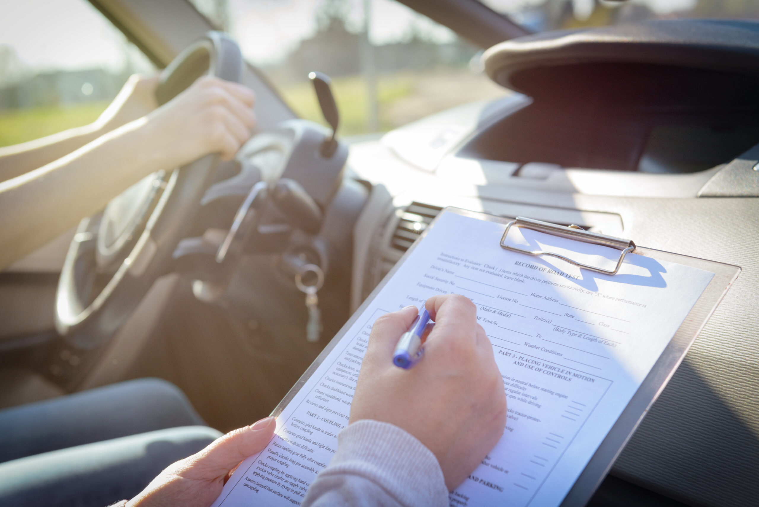 Examiner filling in driver's license road test form sitting with her student inside a car