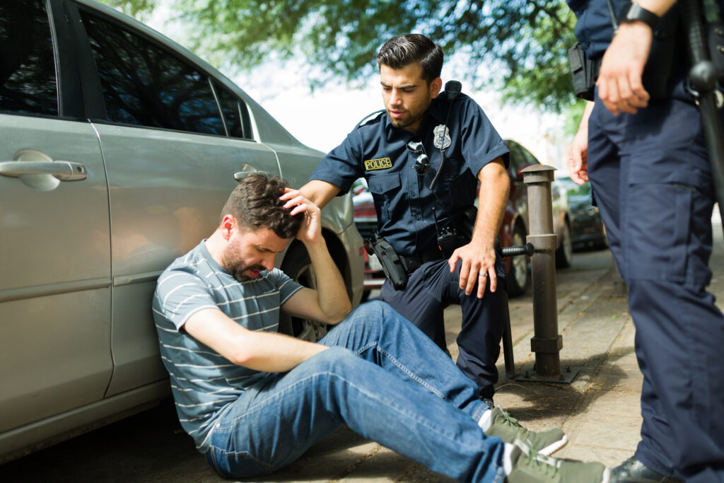 Injured young man suffering in pain after a car accident talking with the police officers. Police report