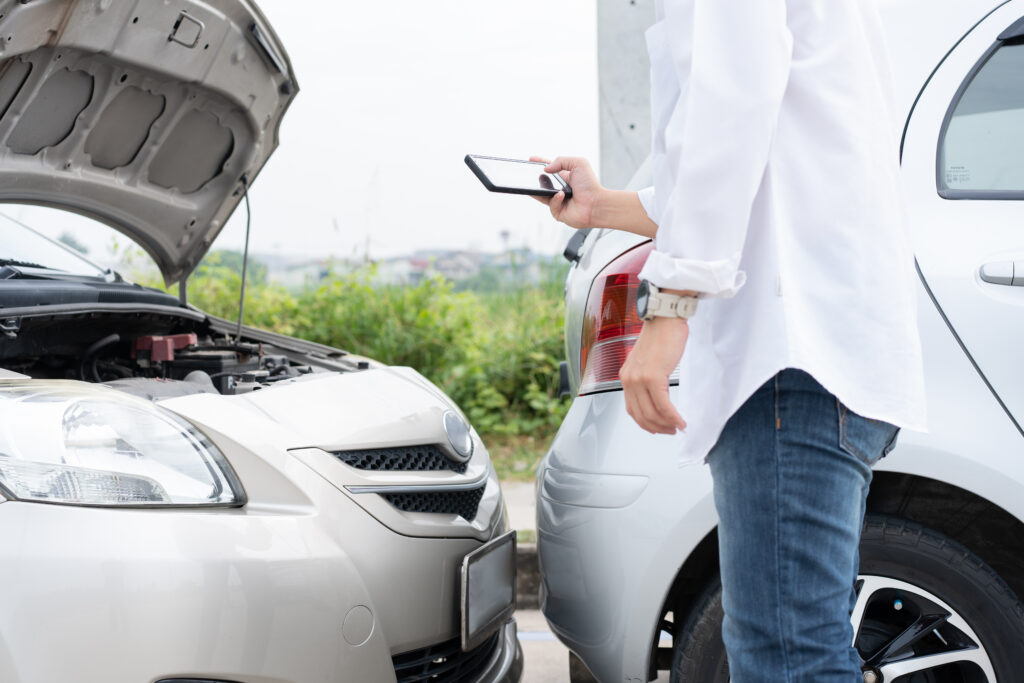 Asian men driver check for damage after a car accident before taking pictures and sending insurance. Online car accident insurance claim after submitting photos and evidence to an insurance company.